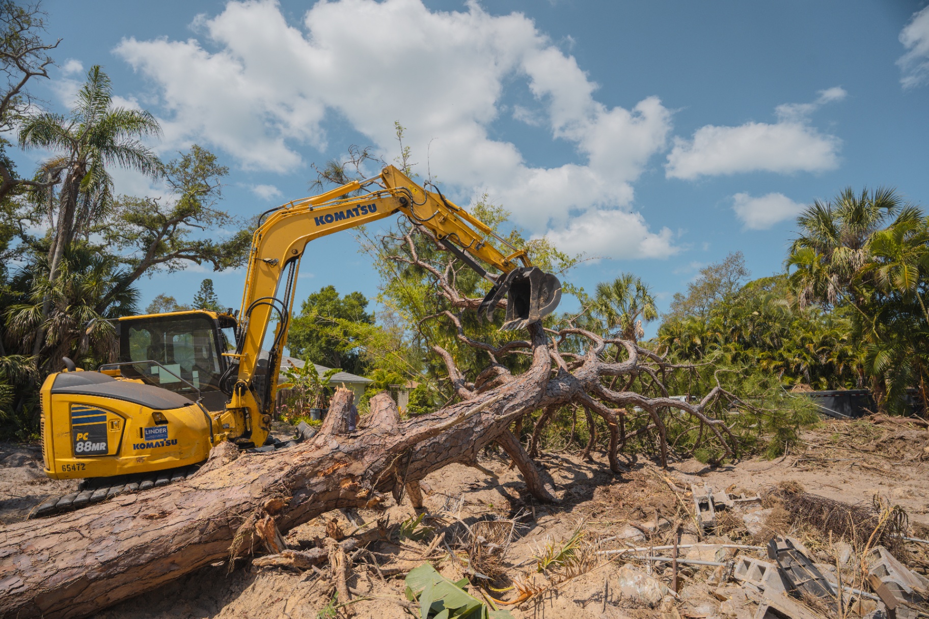 Komatsu excavator lifting large uprooted tree trunk