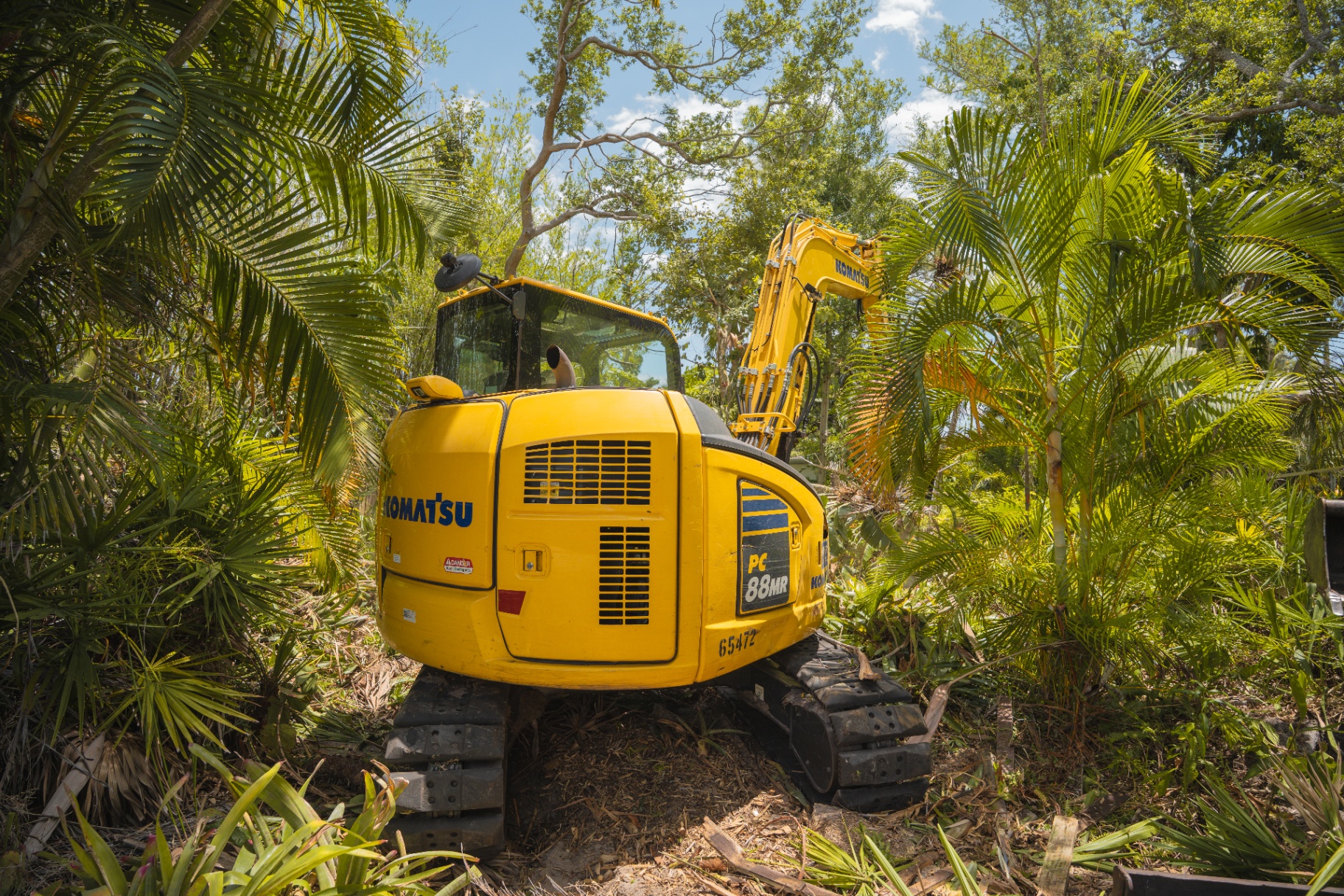 Komatsu excavator working through dense tropical brush