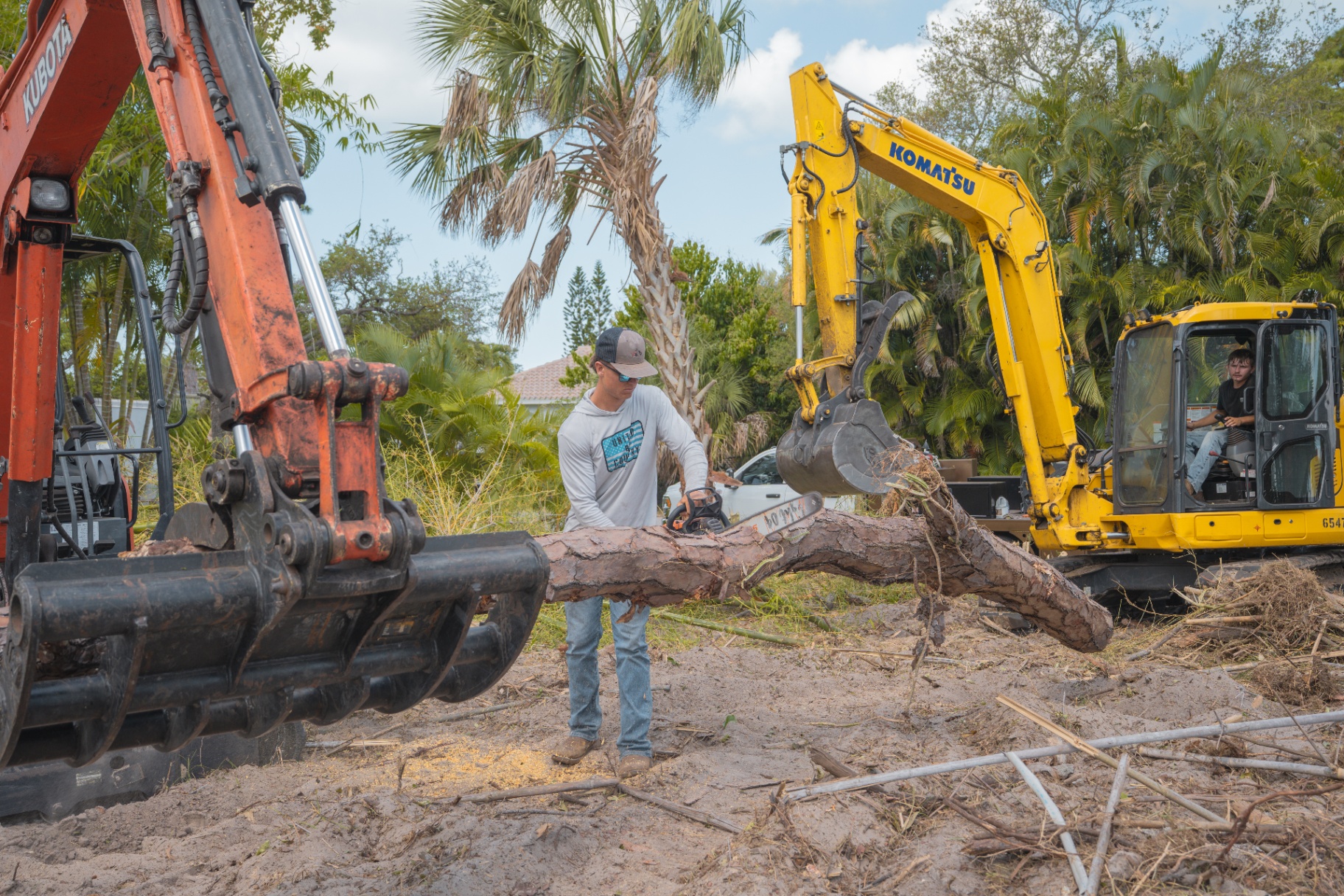Crew cutting fallen tree with chainsaw and excavators